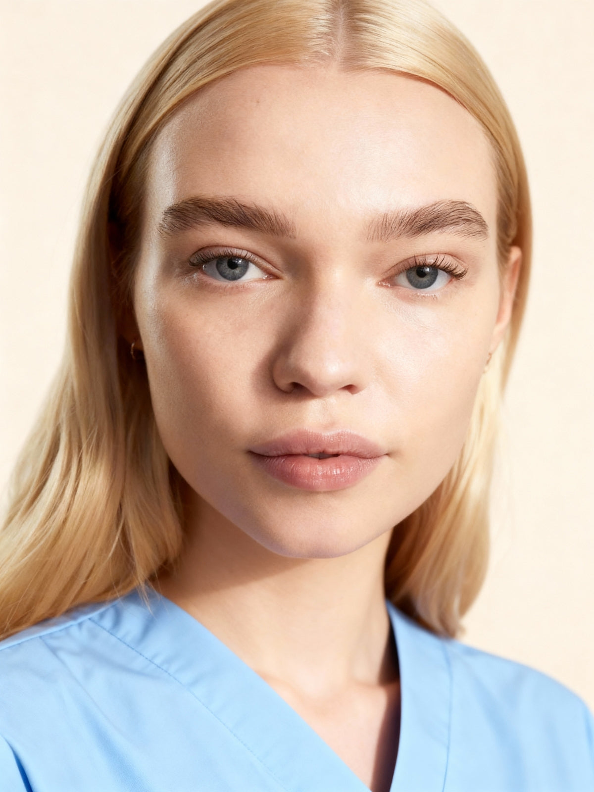 Person wearing a light blue scrub top against a beige background